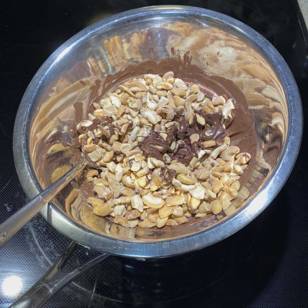 A double boiler with melted chocolates and cashews stirred in.