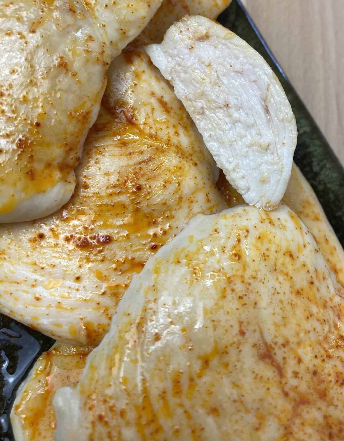 A cross-section of a cooked chicken breast sitting on a pile of more chicken thats seasoned with paprika.