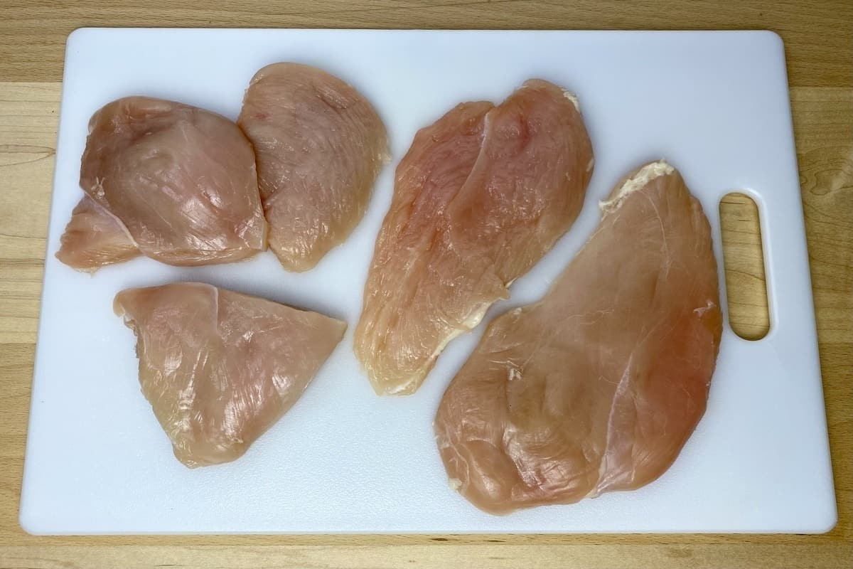 Trimmed chicken breast on a cutting board showing the versions sliced in half and into thirds.