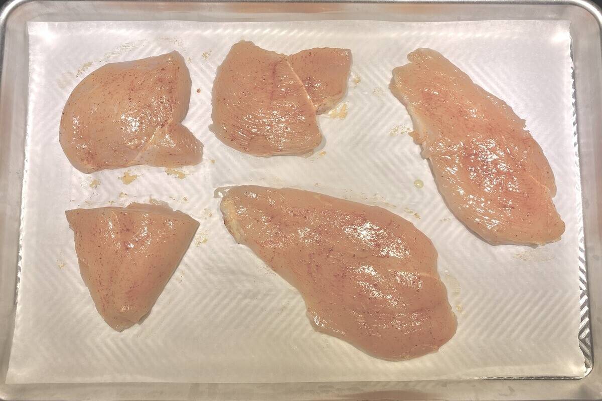 Raw chicken breasts oiled on a lined sheet pan ready for the oven.