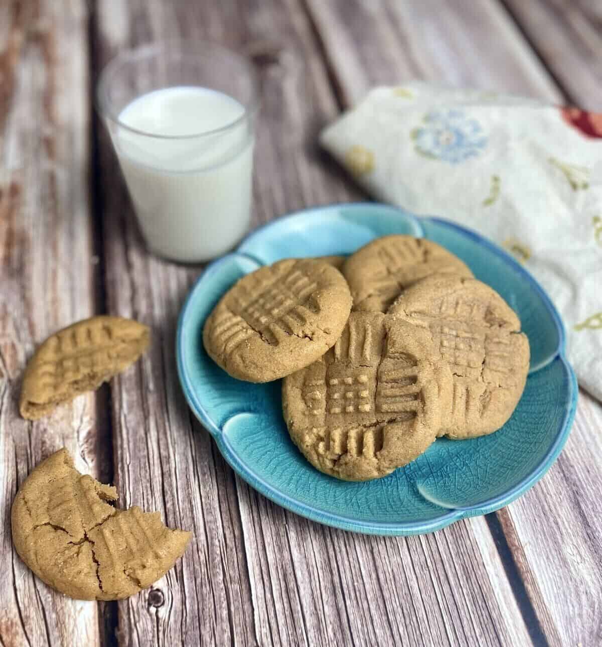 Cookies on a blue plate with a glass of milk and a napkin.