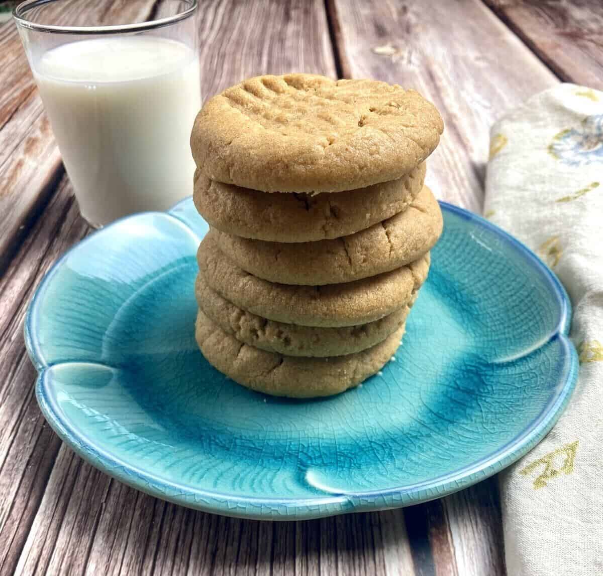 6 cookies stacked up on a blue plate with a glass of milk.