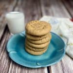 4 ingredient peanut butter cookies stacked up on a blue plate with a cup of milk alongside.