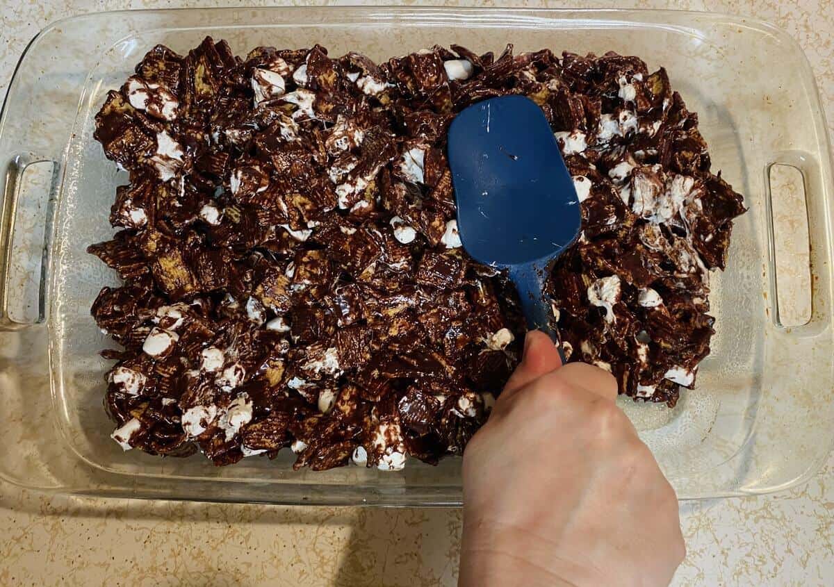 A hand pressing the smores bars into a glass casserole dish with the back of a spatula.