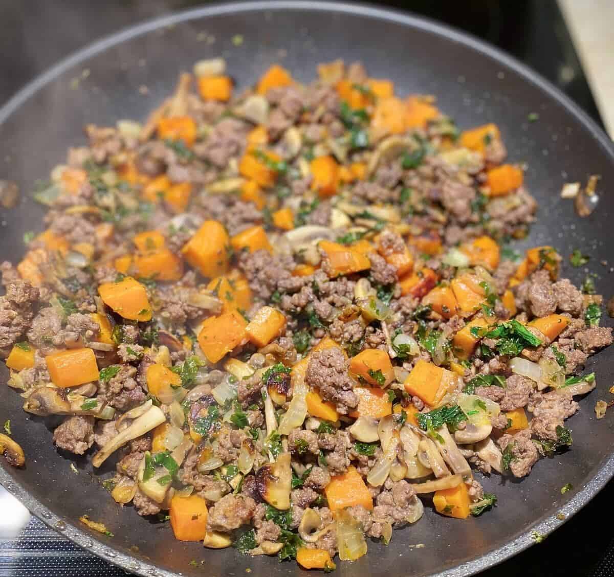 A full batch of steaming cooked hash in the saute pan.