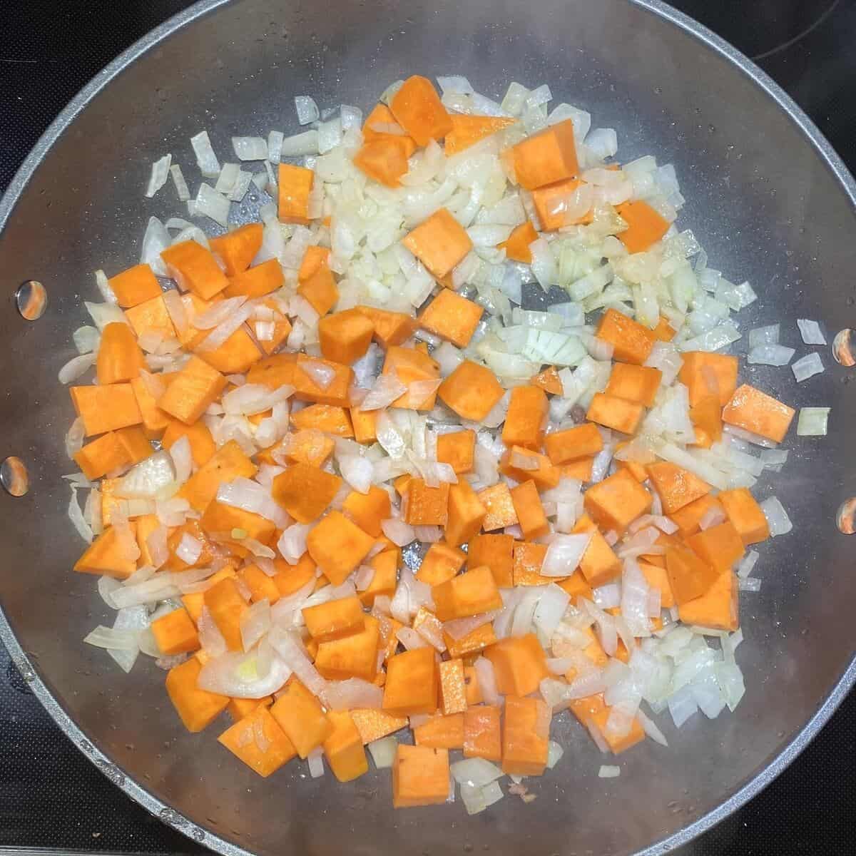 A saute pan cooking onions and yams.