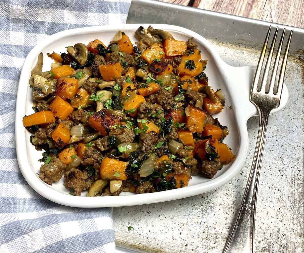 Ground beef and sweet potato hash on a white plate with a fork and a napkin.