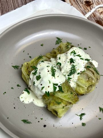 Feature photo for greek cabbage rolls with two rolls on a gray plate beside a napkin.