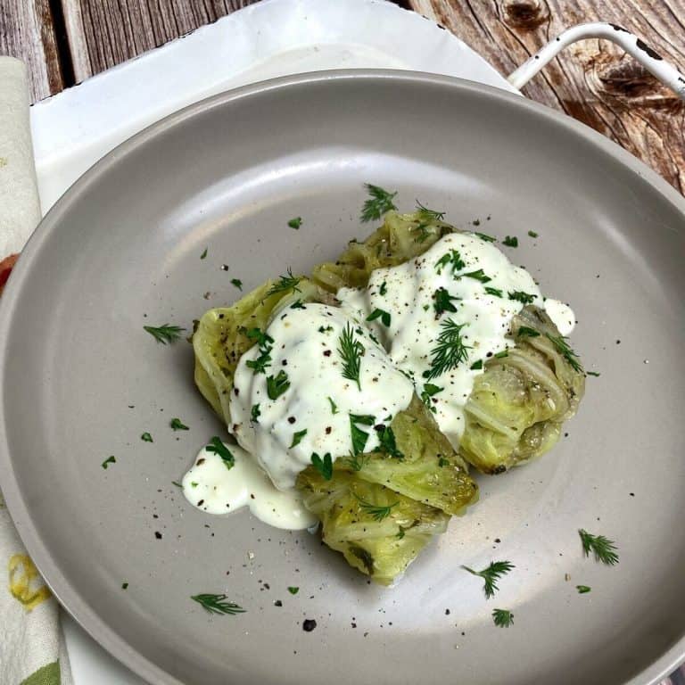 Feature photo for greek cabbage rolls with two rolls on a gray plate beside a napkin.