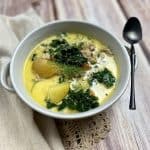 A bowl of chicken kale and potato soup with a spoon.