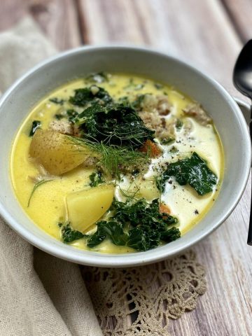 A bowl of chicken kale and potato soup with a spoon.