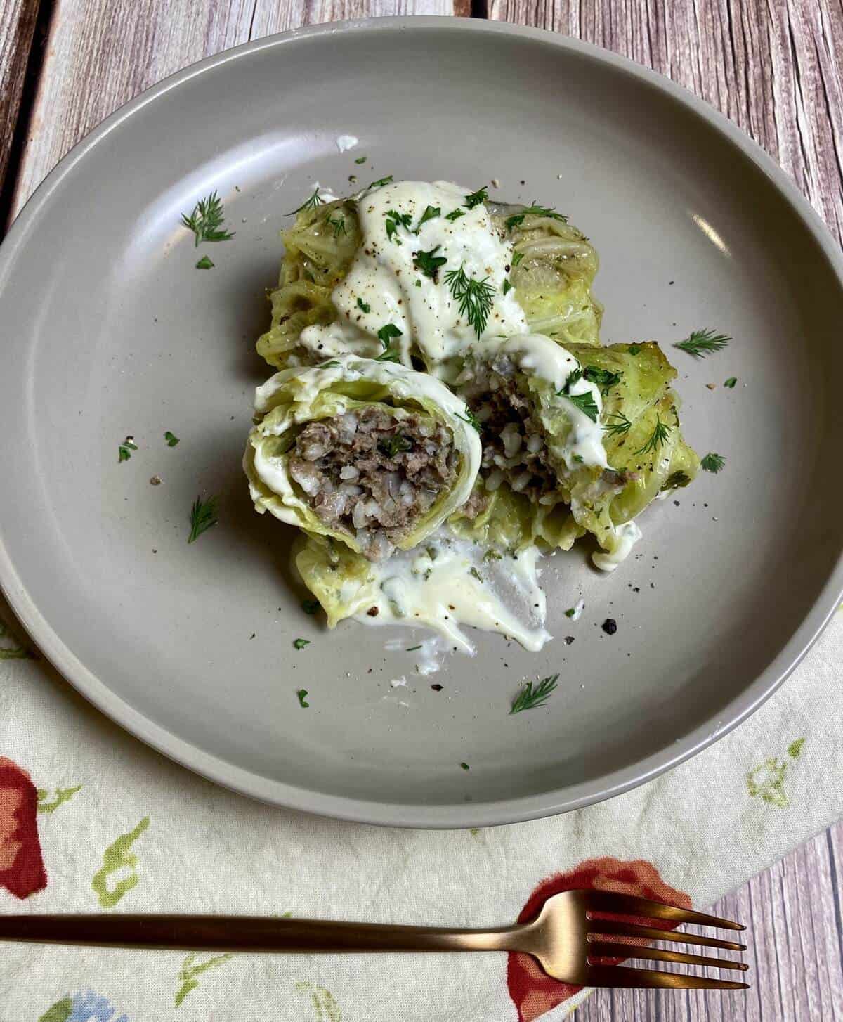 A gray plate with cabbage rolls, but one is cut in half showing the beef and rice interior.