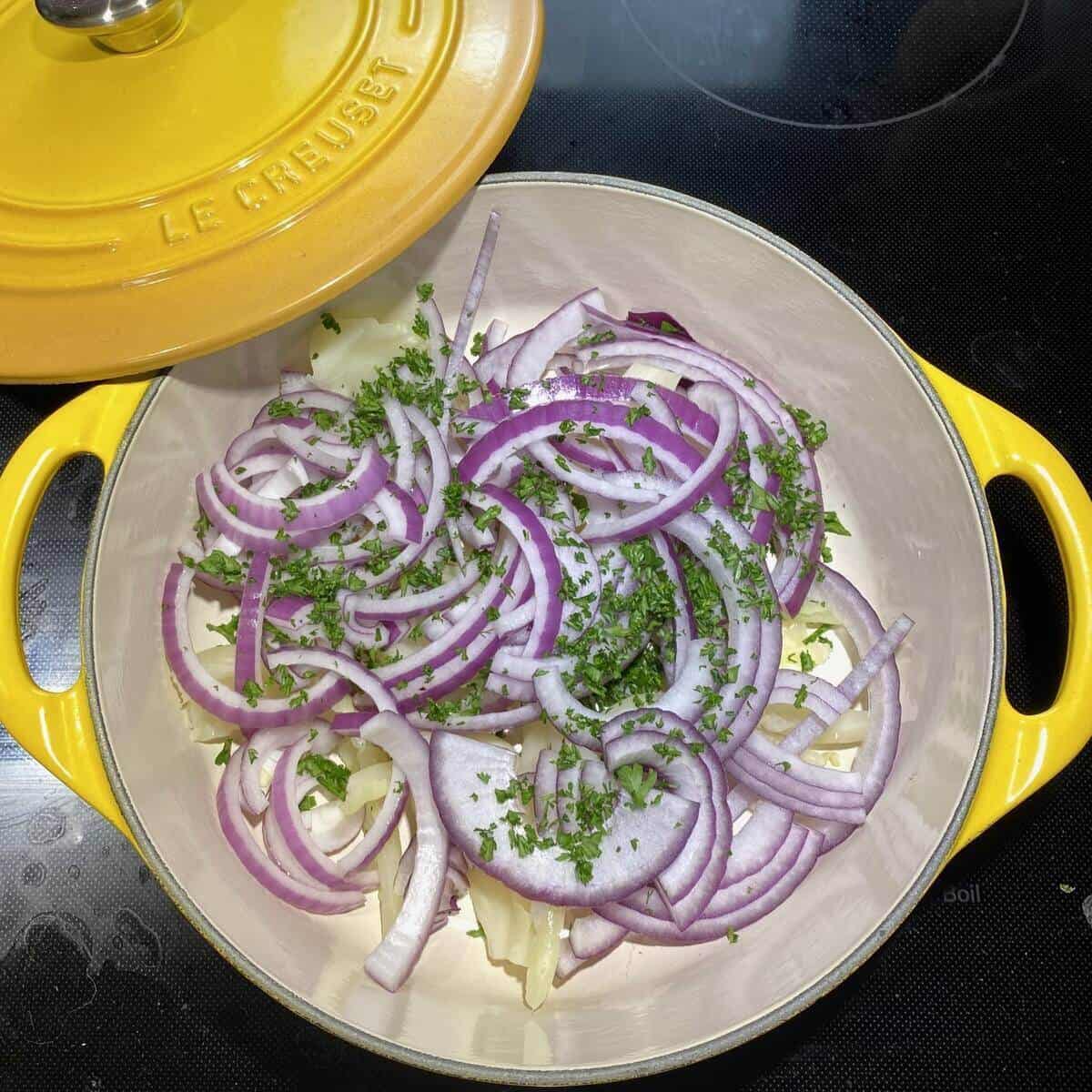 A yellow dutch oven pot filled with the ribs removed from the leaves as well as red onions and herbs.