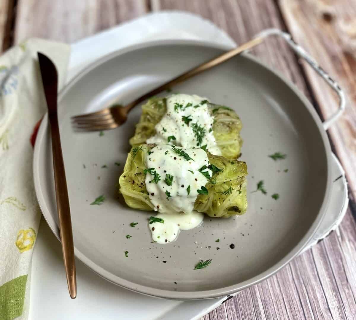 Two cabbage rolls on a plate with silverware and a napkin.