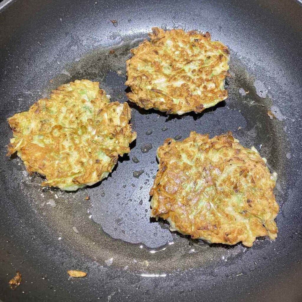 Three fritters in a frying pan when they are done cooking and have browned.