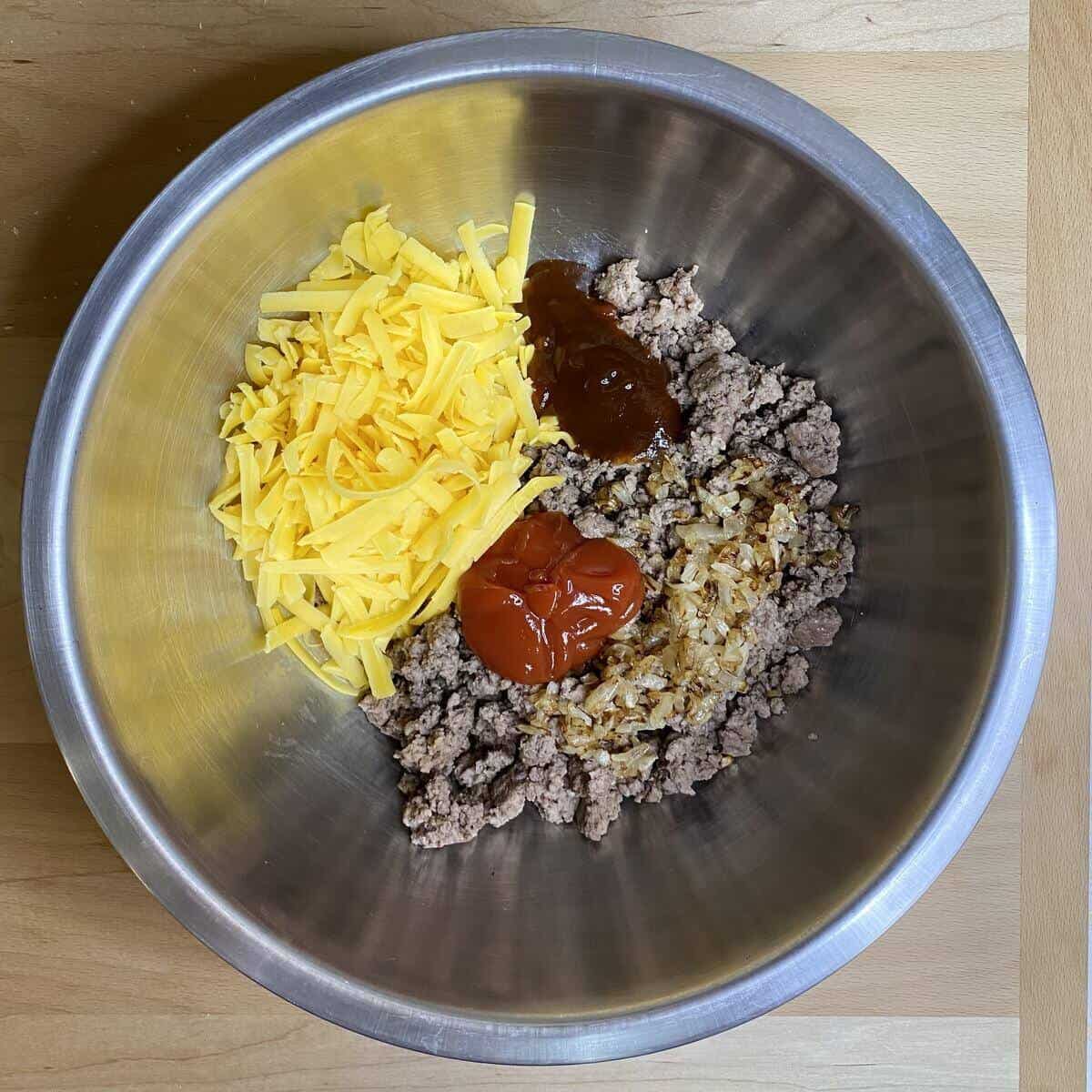 A bowl with ground beef, ketuchup, bbq sauce, and shredded cheddar cheese.