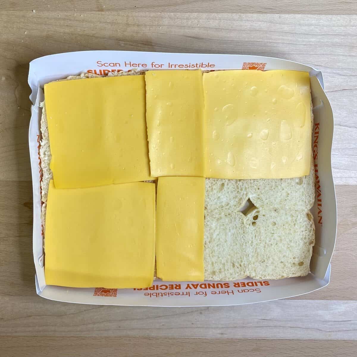 The bottom half of the rolls in the paper tray with american cheese slices.