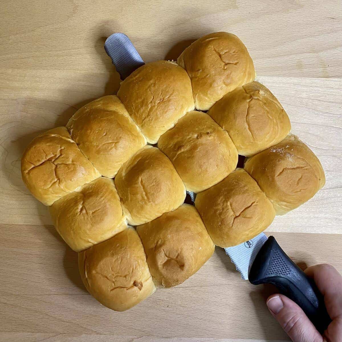 A long serrated knife slicing through the hawaiian rolls horizontally.