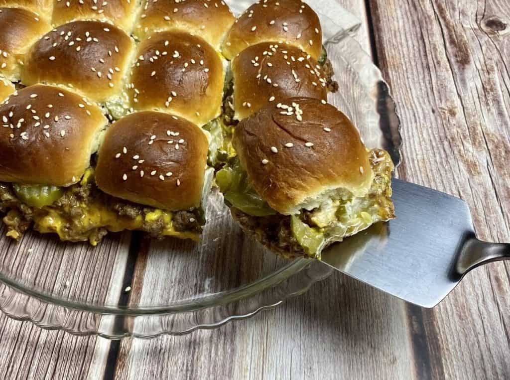 A platter of cheeseburger sliders with one being lifted out with a spatula.