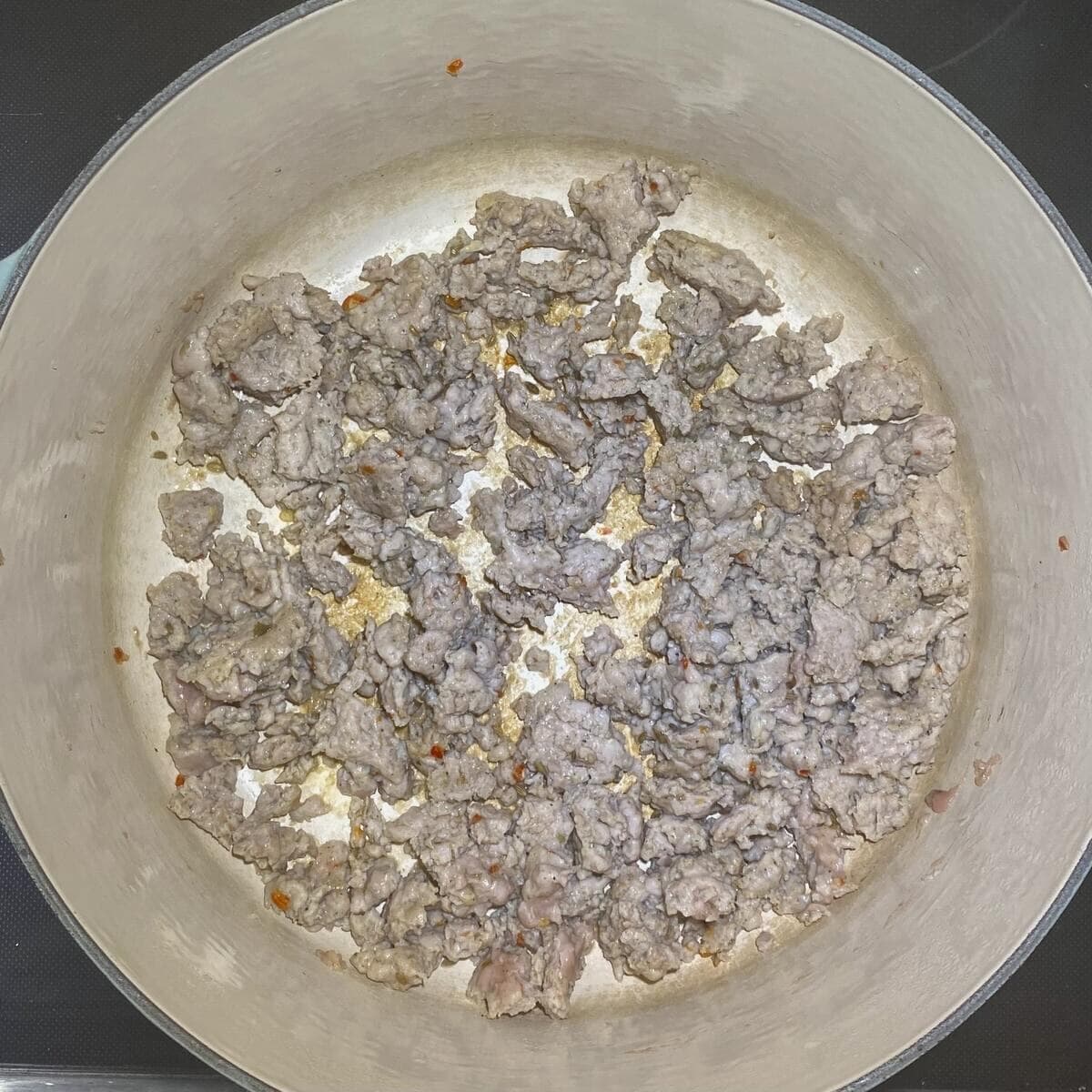 A large pot on the stove browning the chicken sausage.