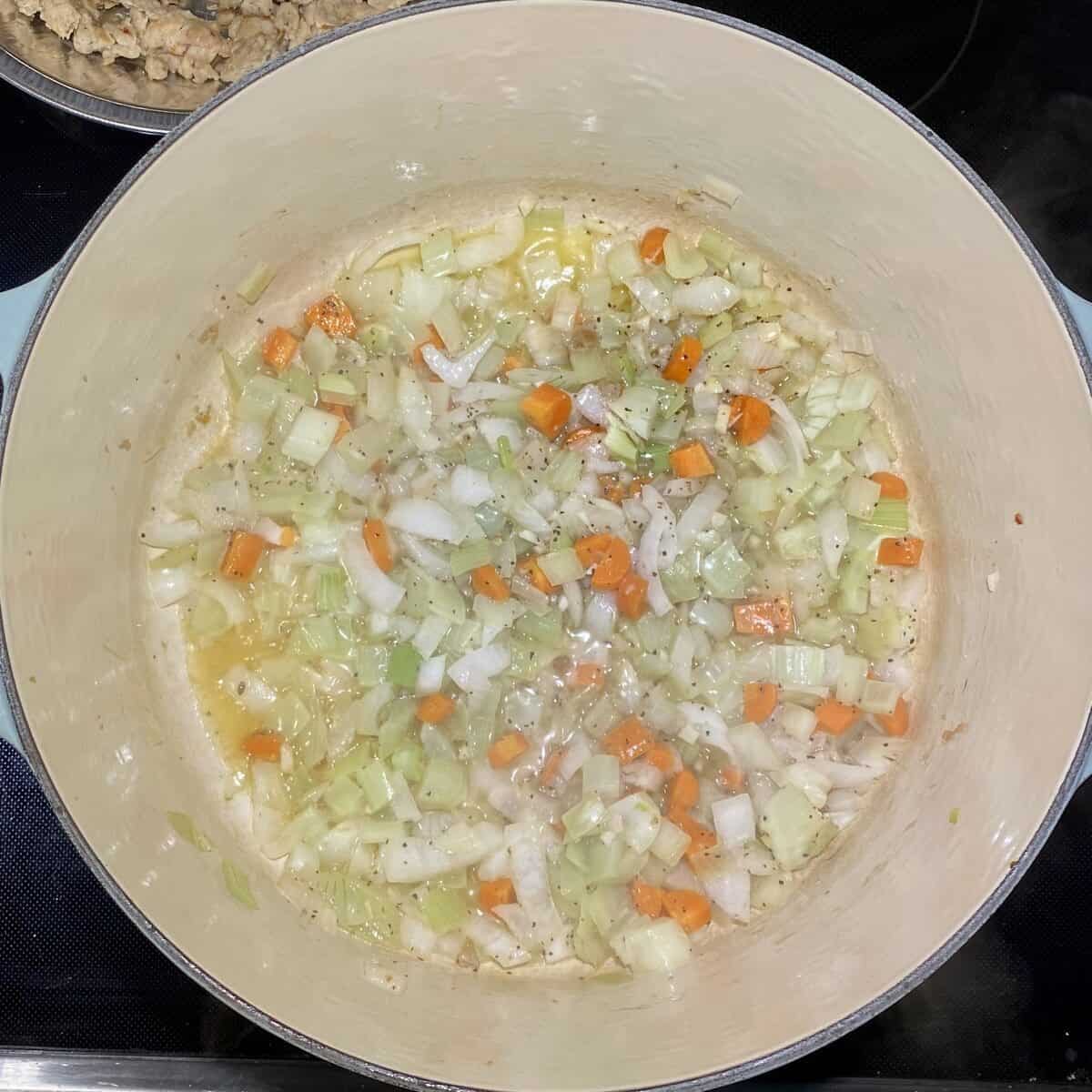 A large pot on the stove simmering vegetables in butter with the chicken sausage on a plate off to the side.