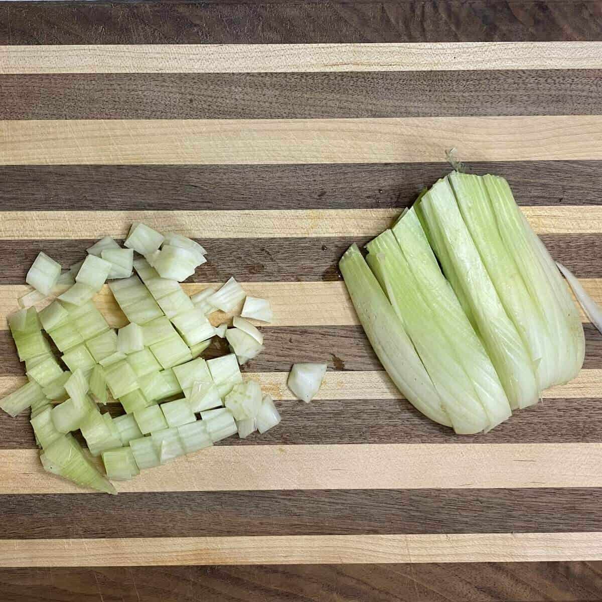 A cutting board with a fennel bulb sliced in half with one half diced and the other sliced into sticks.