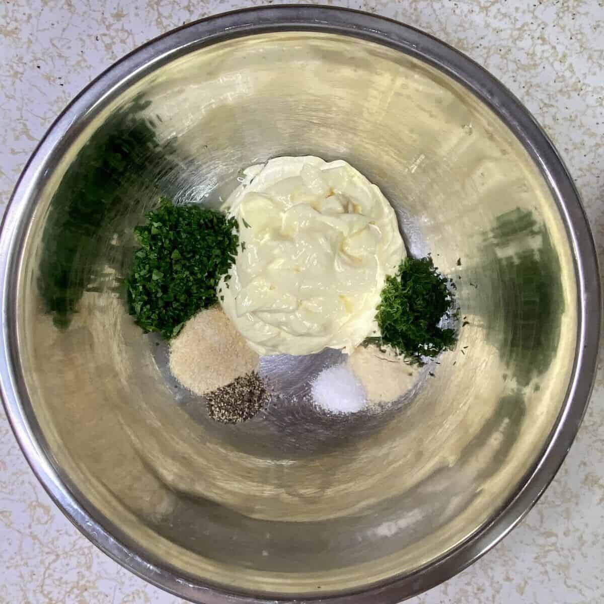 A stainless steel bowl with all the ingredients for making the dressing except buttermilk.