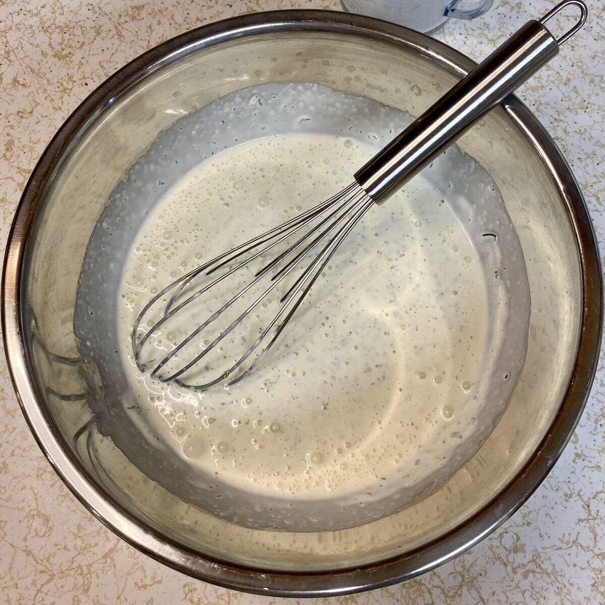 A stainless steel bowl with a whisk holding the finished ranch dressing.