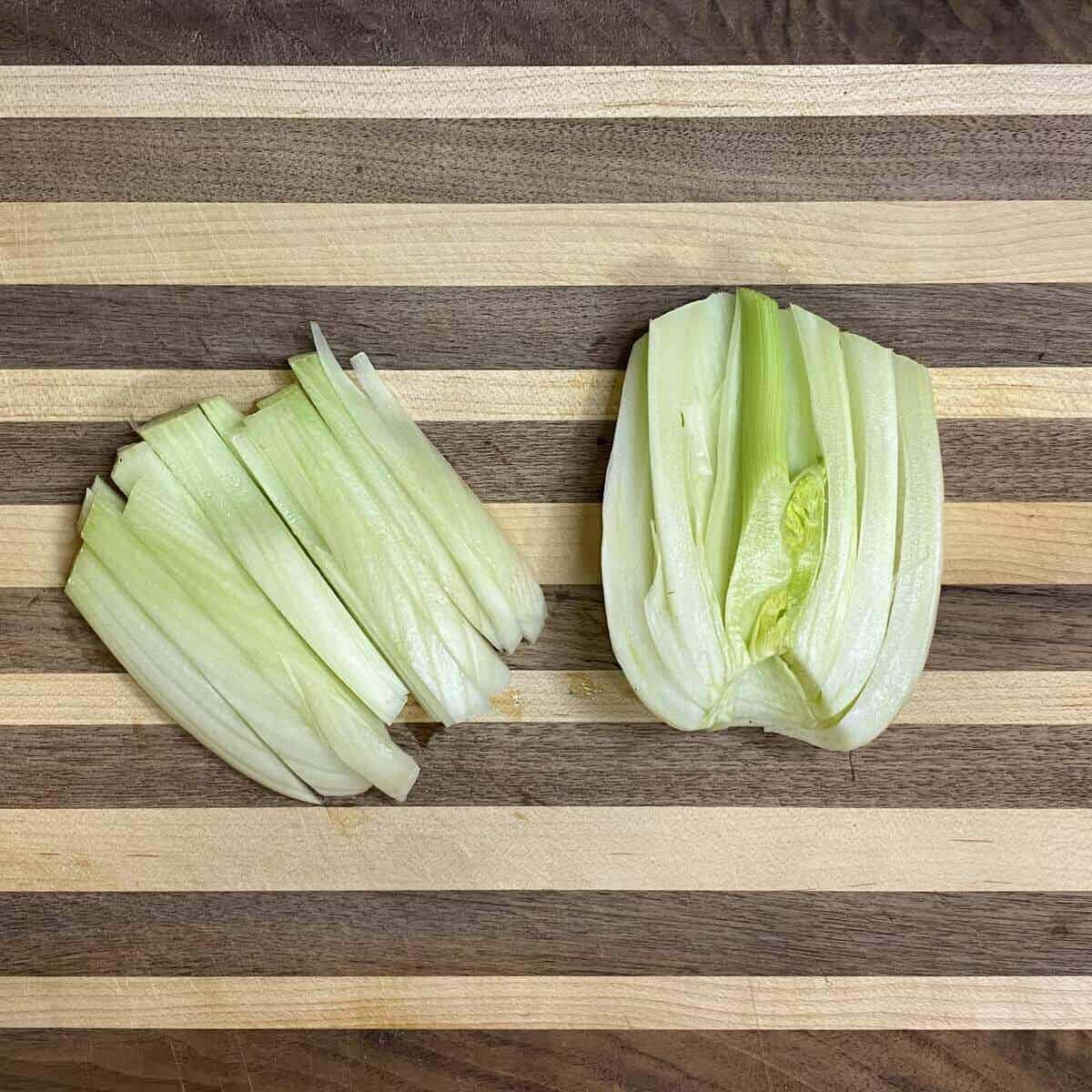 A fennel bulb on a cutting board sliced in half and one half is sliced into sticks.