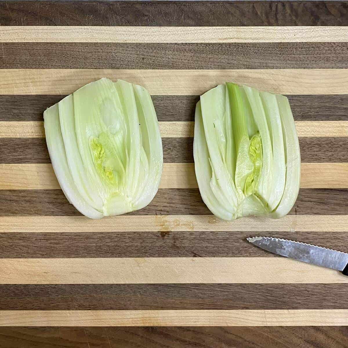 A fennel bulb on a cutting board sliced through the core with some core removed.