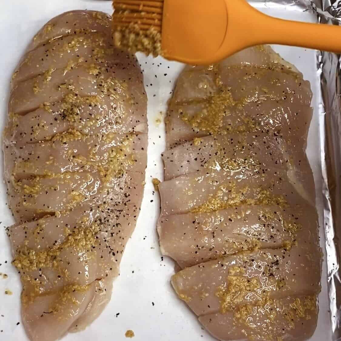 A basting brush above two hasselbacked chicken breasts on a sheet pan.