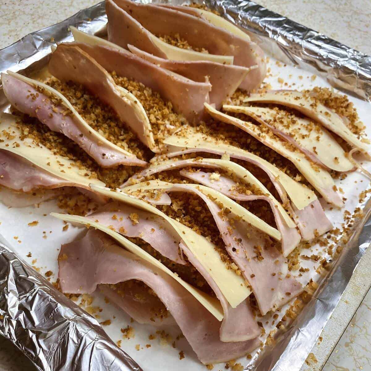 A side view of the finished pan of raw hasselbacked chicken stuffed with ham and cheese.