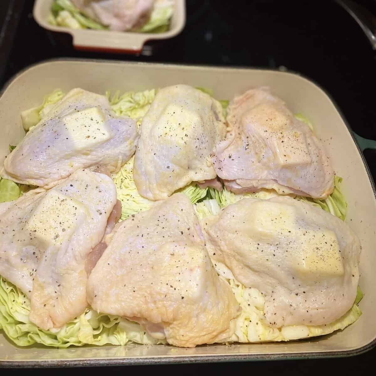 Raw chicken thighs with butter pats tucked under the skin on top of cabbage.