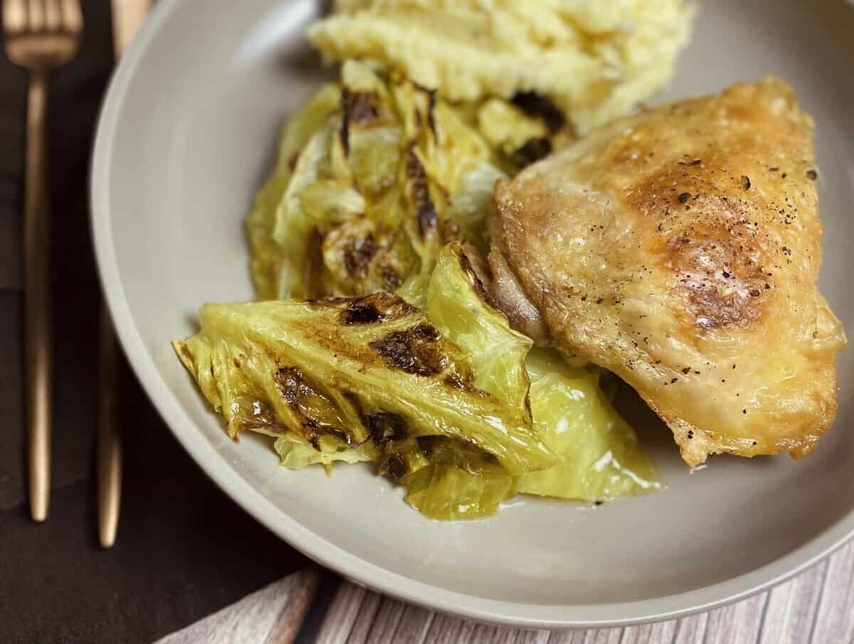 Cooked cabbage and chicken on a dish with silverware.