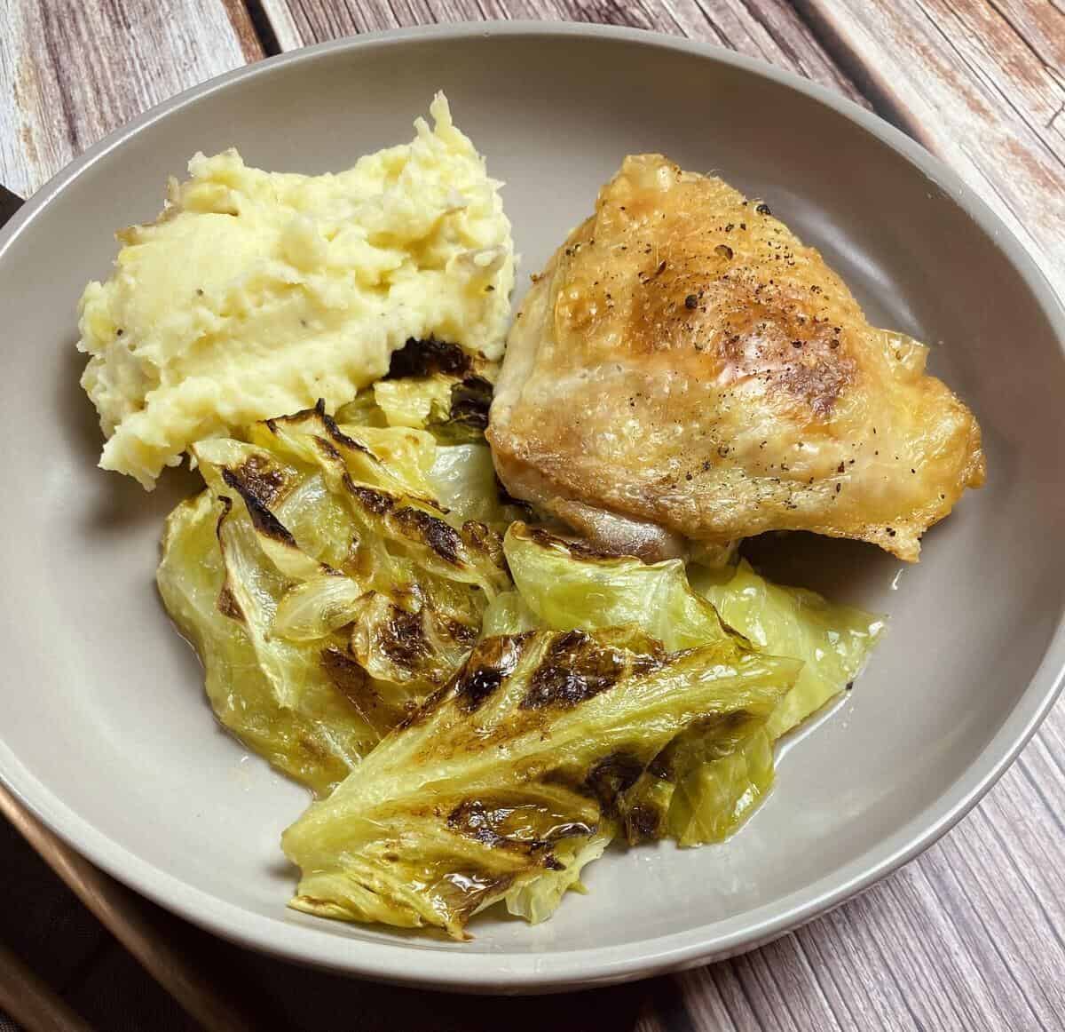 A plate with a crispy cooked chicken thigh and schmaltzy cabbage with potatoes.