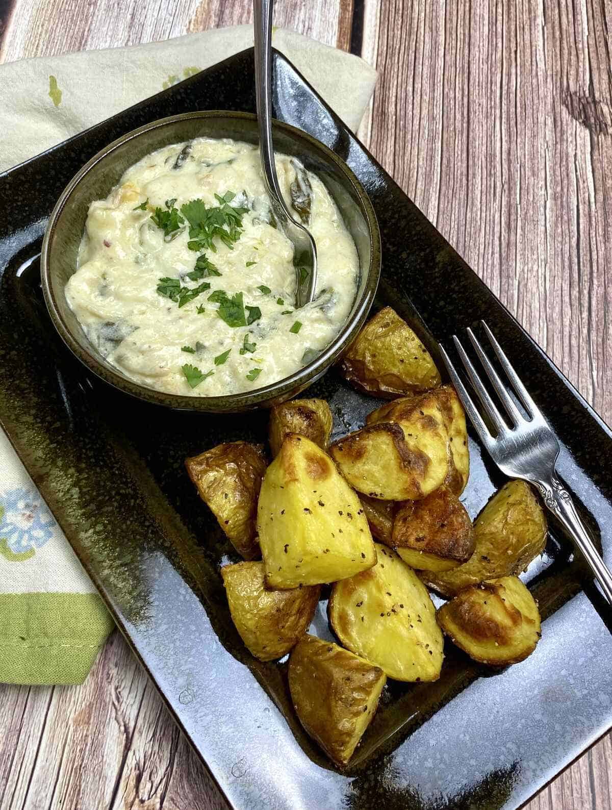 A small dish holding crab and spinach dip with a side of roasted potatoes.