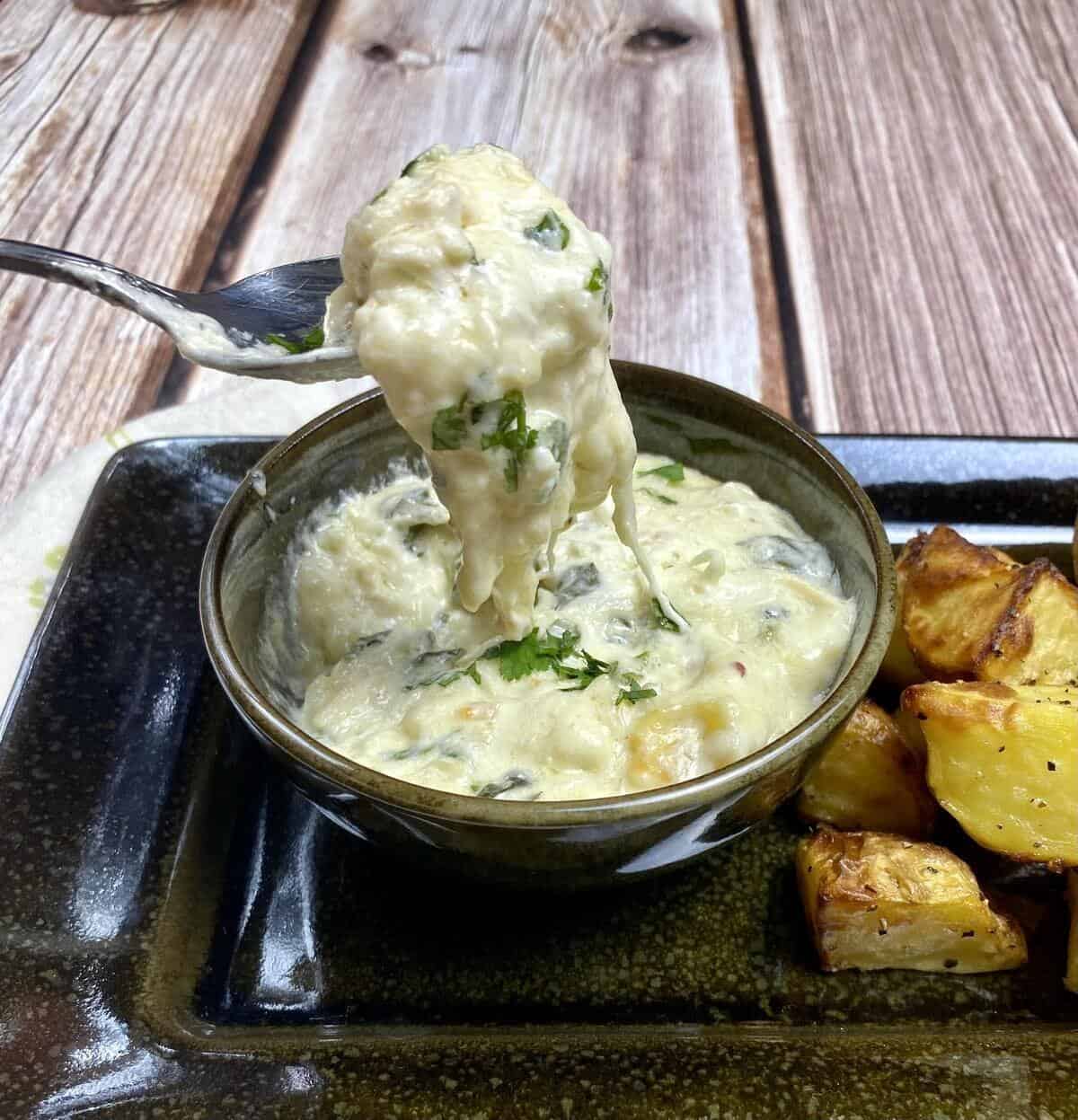 A spoon dishing out a bite of hot dip from a small bowl alongside fried potatoes.