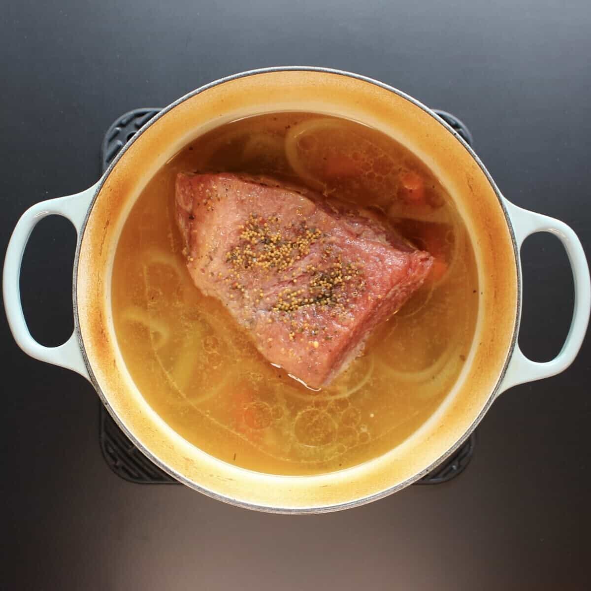 A dutch oven holding cooked vegetables, corned beef, and broth.