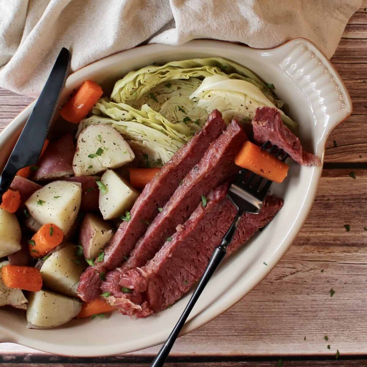 Slices of roasted corned beef on a plate with vegetables and silverware.