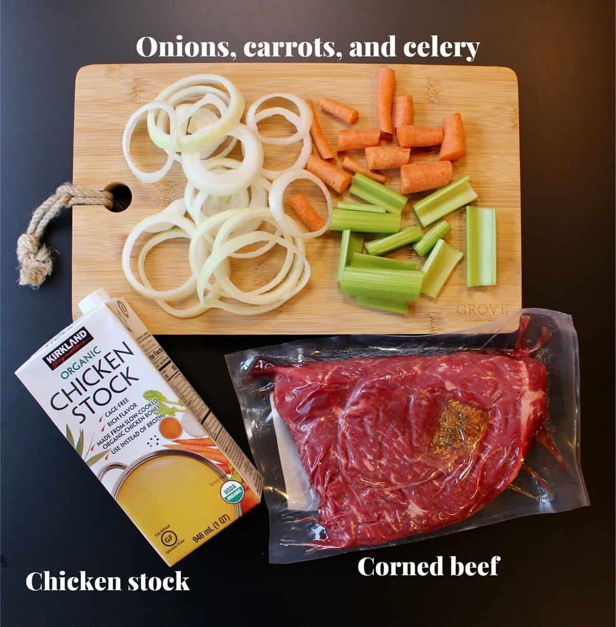 A cutting board with chopped vegetables, an uncooked corned beef next to it alongside a box of chicken stock.