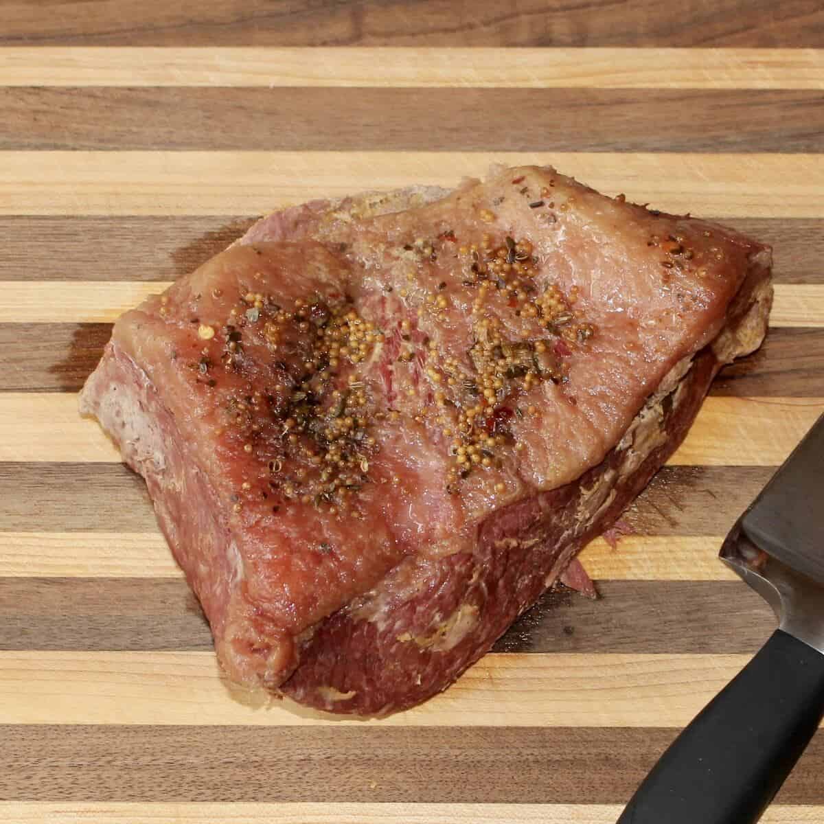 A roasted corned beef on a cutting board with a sharp knife.