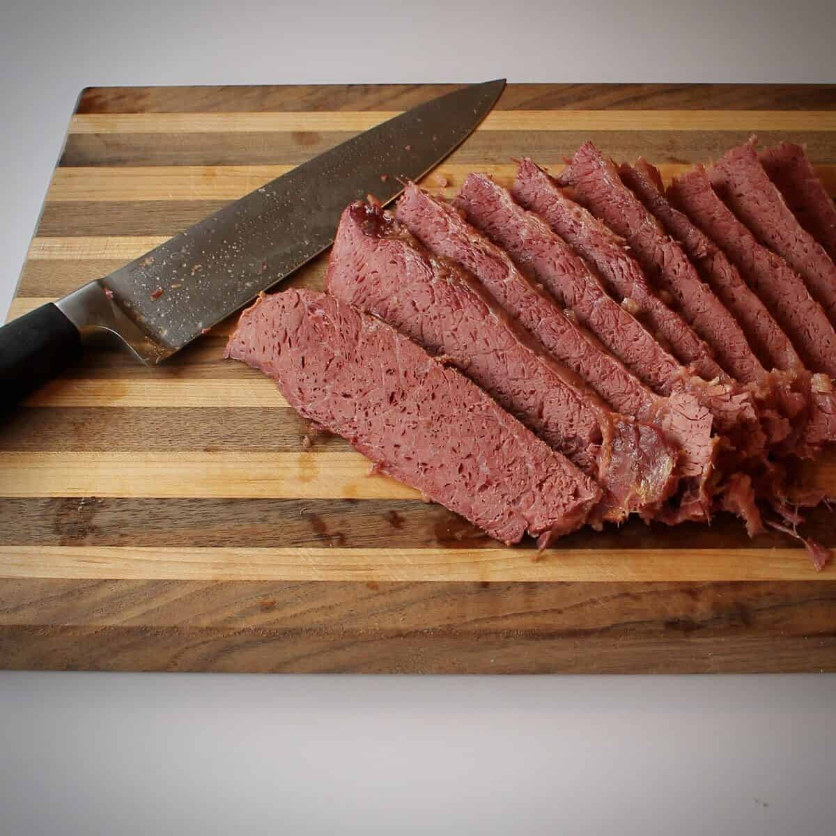 A roasted corned beef on a cutting board with a knife after it has been sliced.