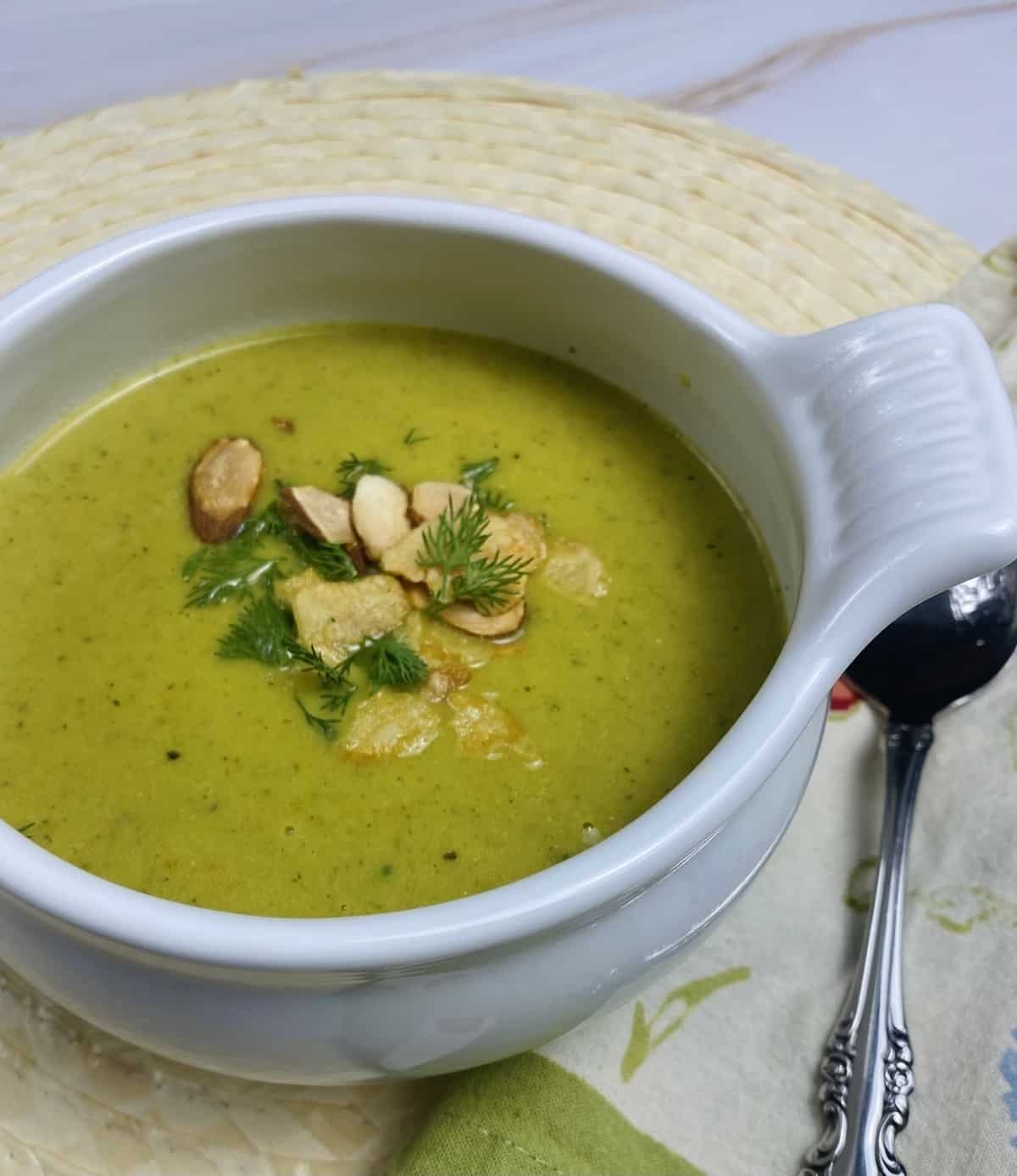 A bowl of asparagus and broccoli soup with crunchy toppings and dill.