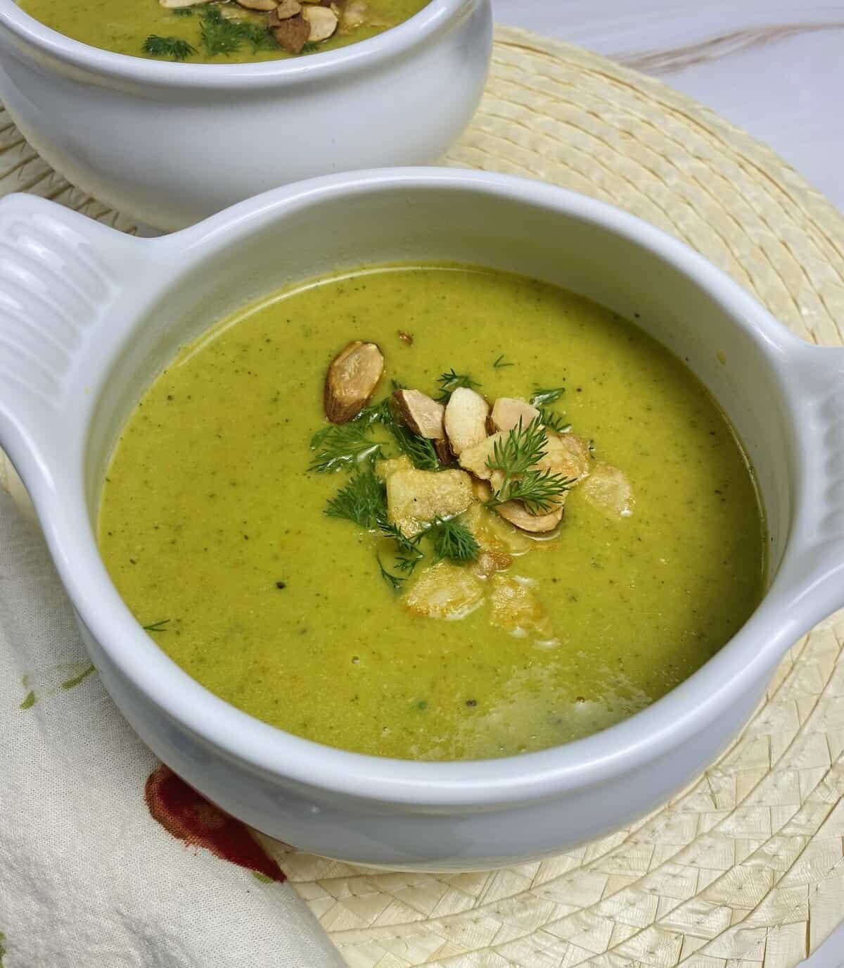 A bowl of green blended soup with crunchy toppings and dill.