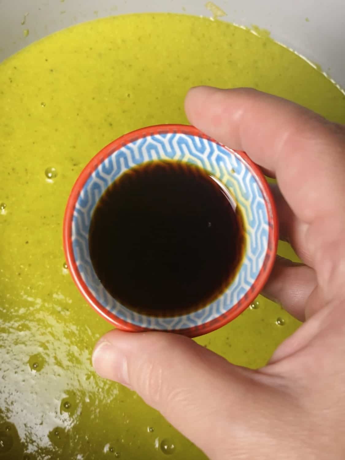 A small bowl of soy sauce above a pot of blended asparagus and broccoli soup.