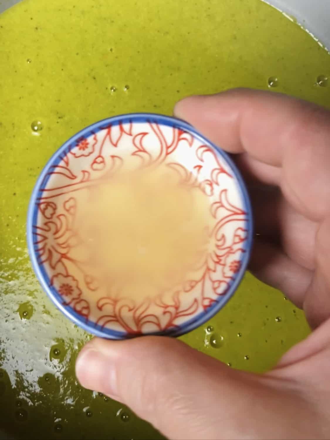 A small bowl of lime juice above a pot of blended asparagus and broccoli soup.