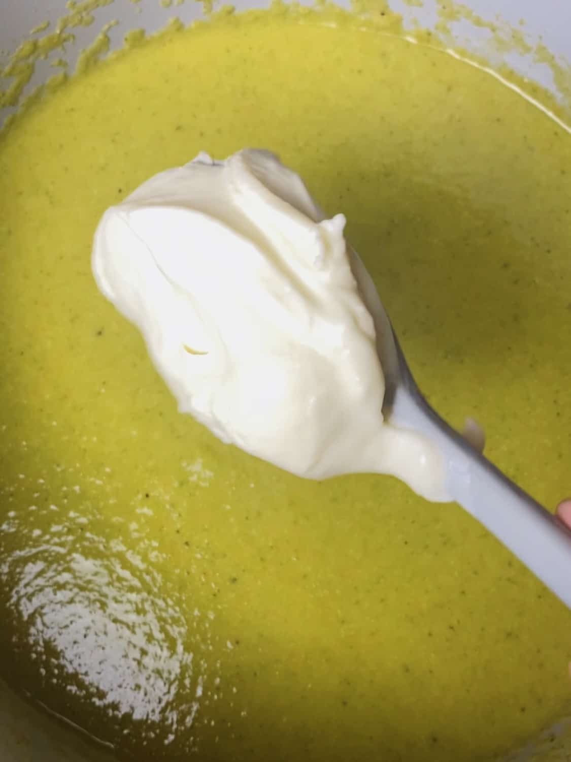 A spatula with creme fraiche about to be stirred into a pot of soup.