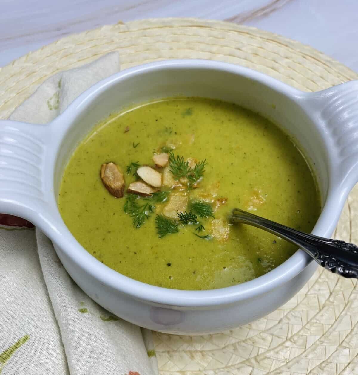 A spoon in a bowl of asparagus soup on a placemat with a napkin.