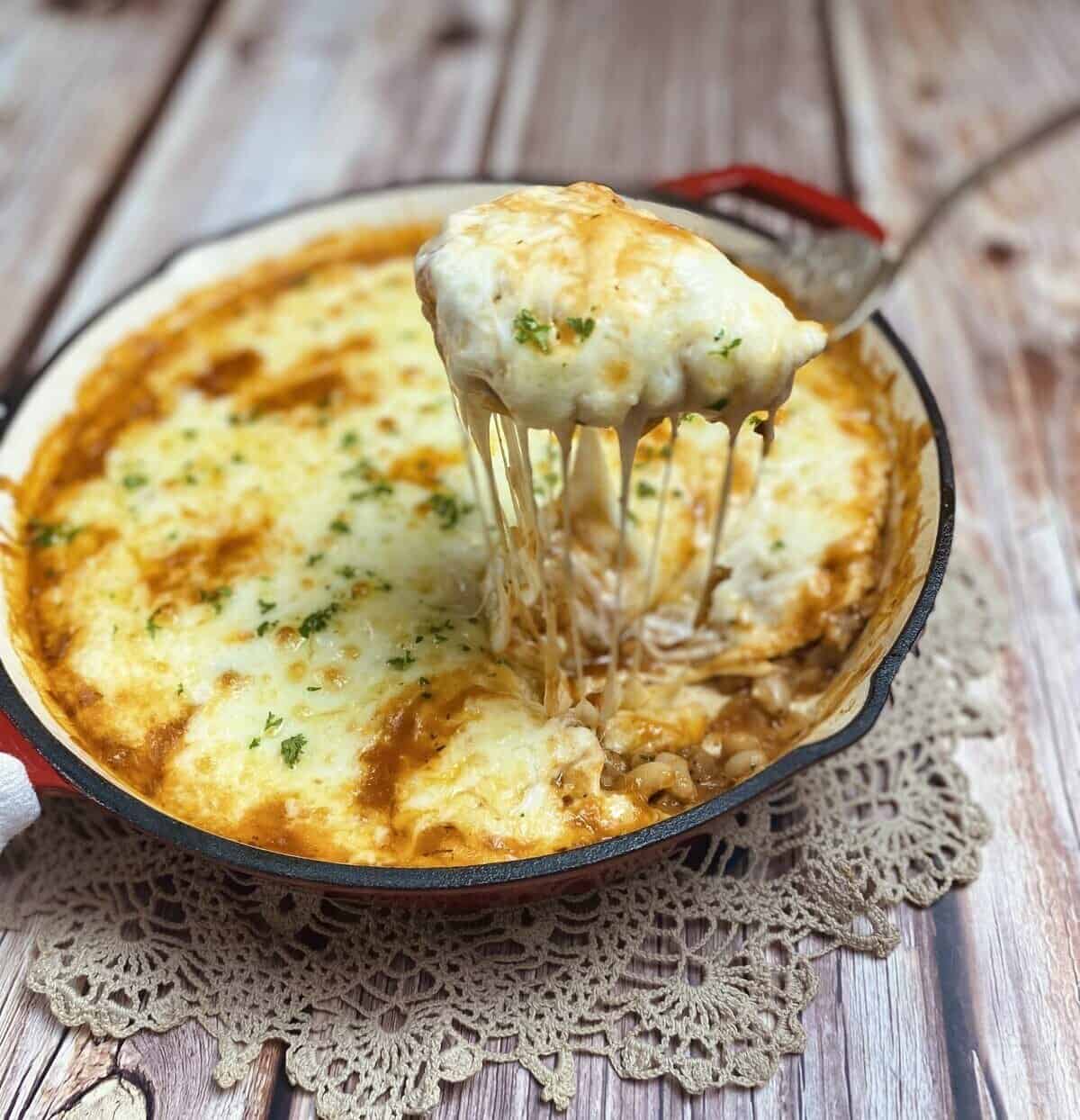 A serving spoon pulling a scoop of cheesy bean tomato bake up from the skillet.