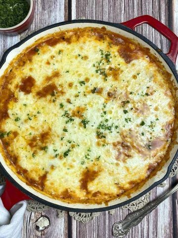 Cheesy white bean tomato bake cooked in a skillet alongside a towel and spoon.